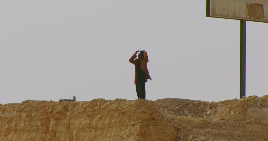 Model man fixing his hair while standing on a dirt hill next to an overpass