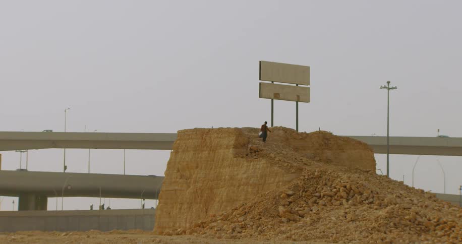 Man in a ravine going down next to an overpass with vehicle traffic