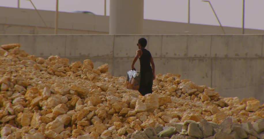 Man with a bag climbing a hill of rocks next to an overpass