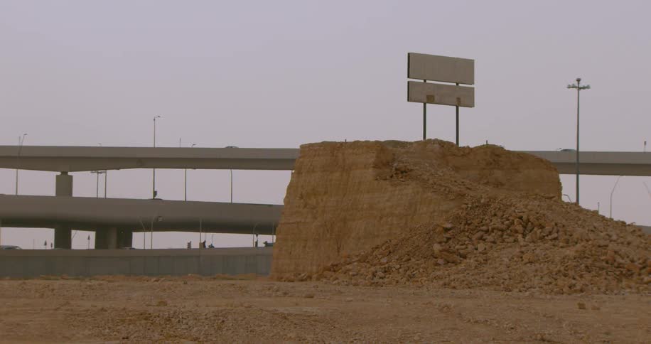 A giant dirt mound sits near overpasses filled with traffic