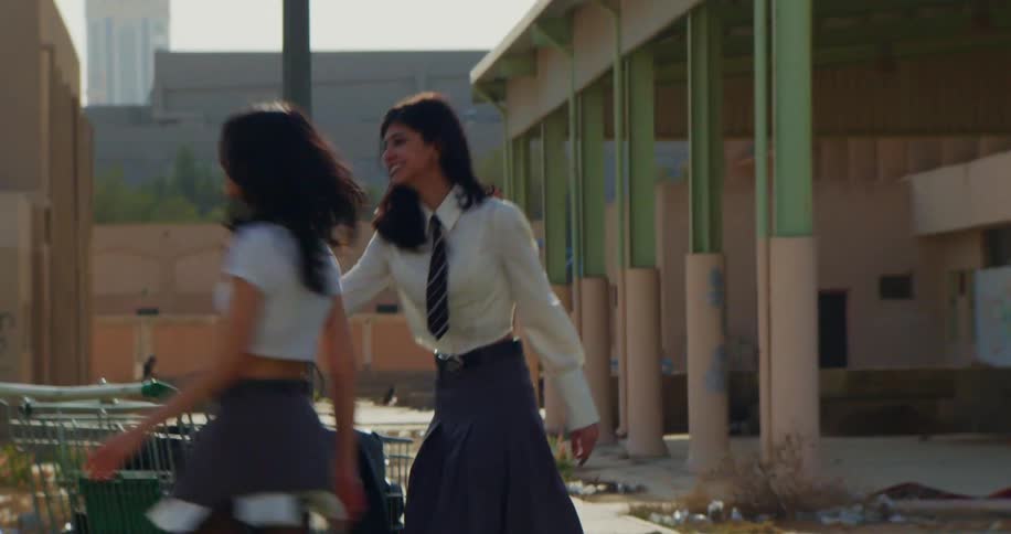 Two teenagers in school uniforms playing with a shopping cart outside an abandoned building