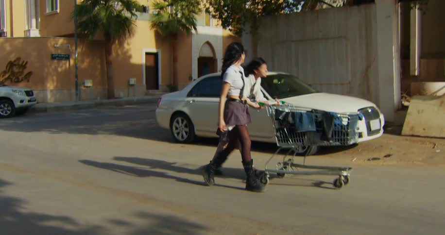 A girl pushes a grocery cart while walking and laughing with her friend