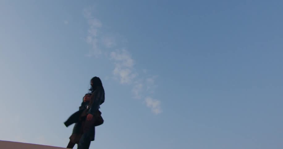 A couple walking on a rooftop under a blue sky