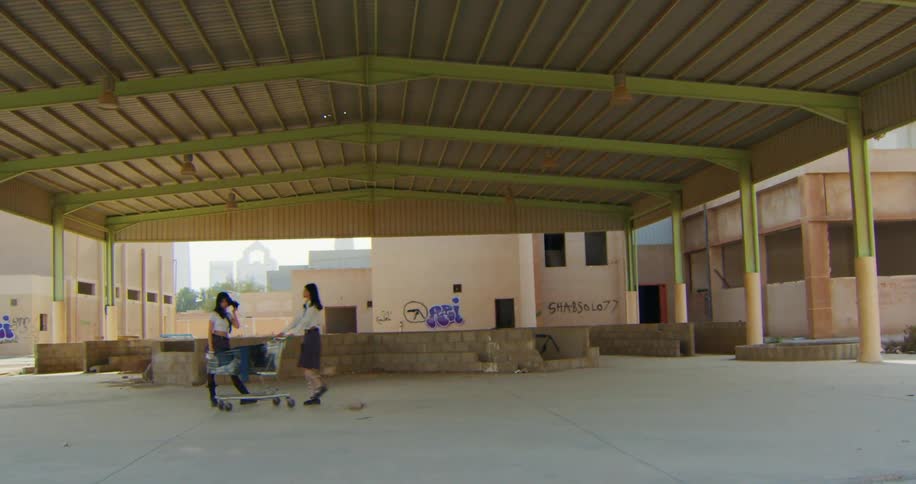Two uniformed women in the same clothes carrying a shopping cart in an open warehouse