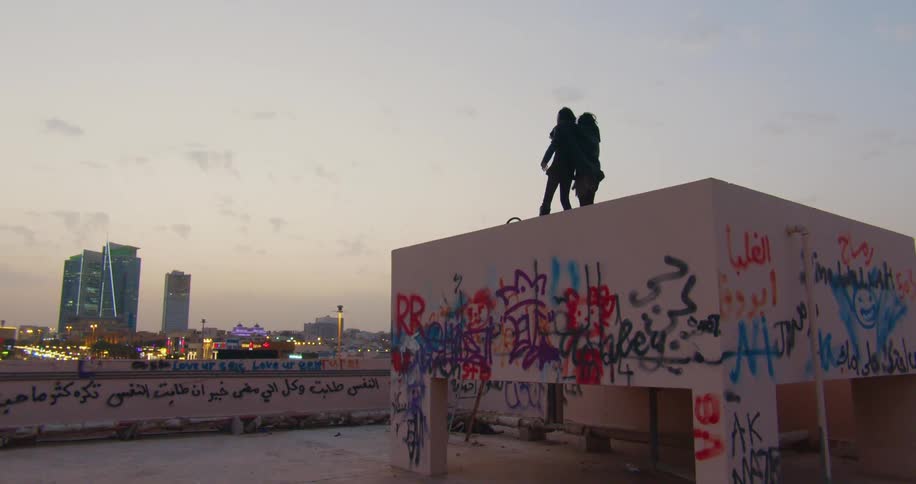 A silhouette of two people hugging each other and they are on top of a building that is full of graffiti and they are seeing the city on the horizon