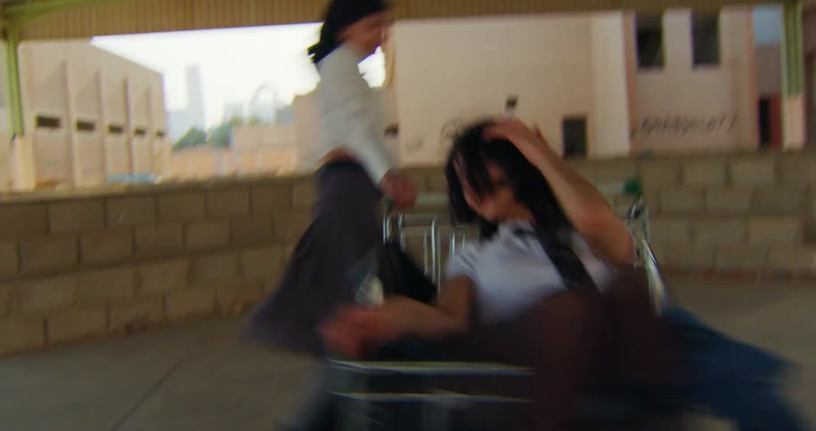 Two women on top of a supermarket trolley rotating in a warehouse