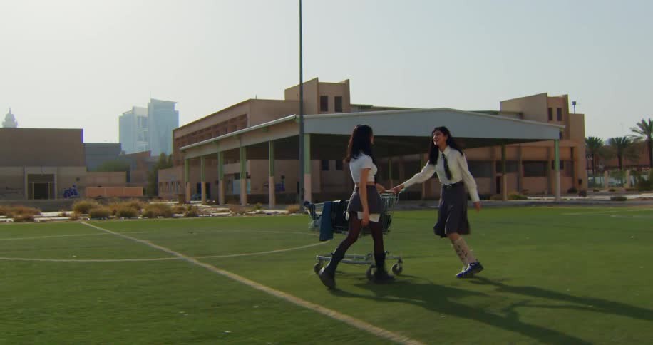 Two girls in school uniforms pushing a cart on a soccer field