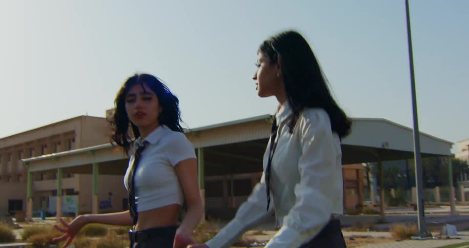 Teenagers smile and talk while walking with a shopping cart across turf near building