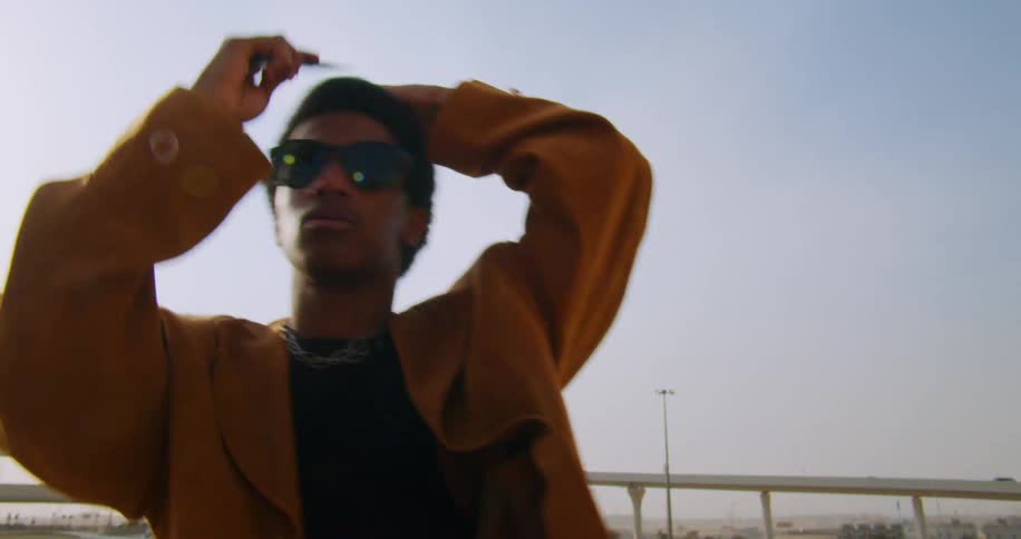 Model man adjusting his hair and clothes while wearing sunglasses outdoors in the open air