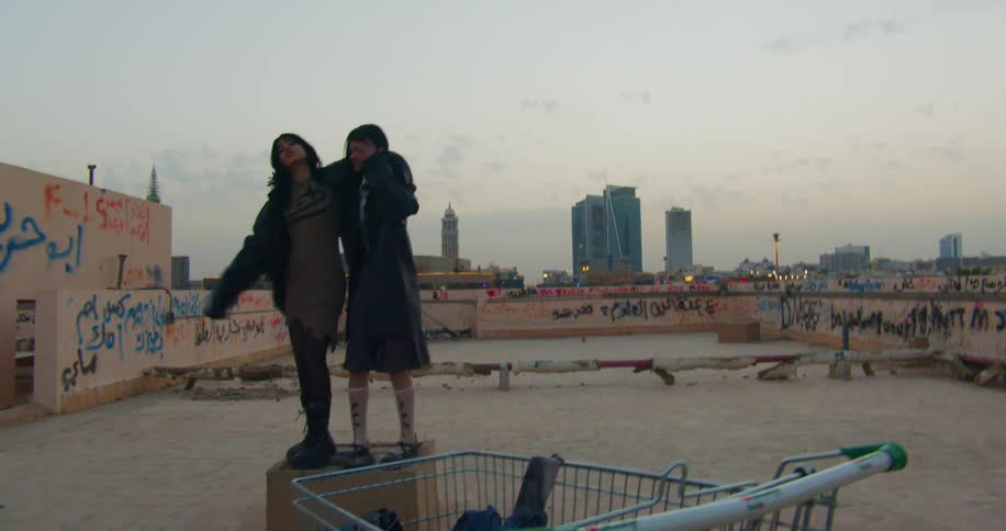 Two teenage girls stand on a rooftop near the city at sunset