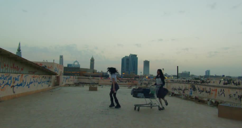 A couple of teenagers dressed as schoolgirls play with a shopping cart on the roof of a building