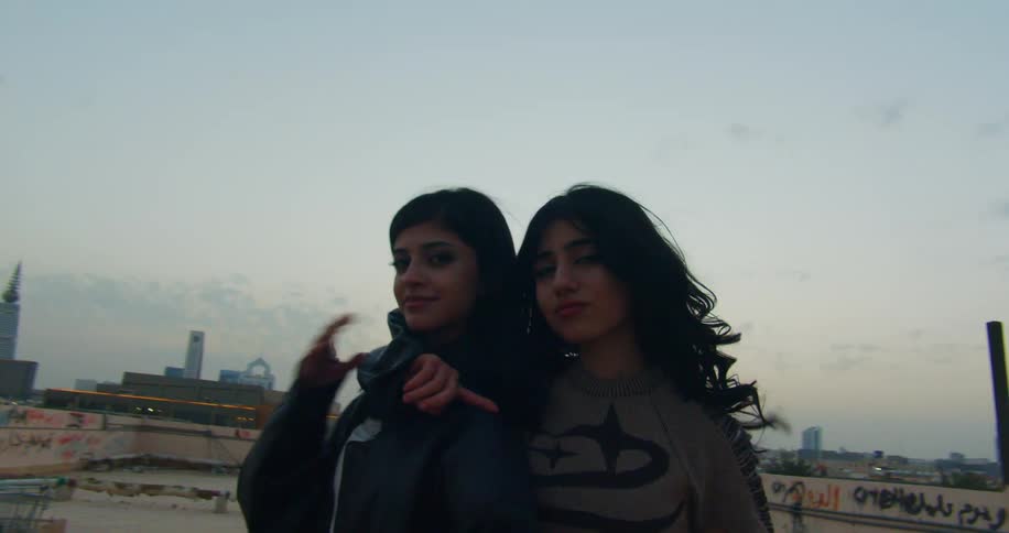 Two models walking on a terrace of a building with skyscrapers in the background