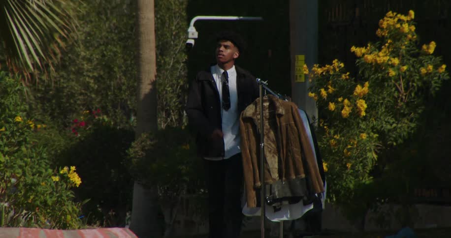 Man walking alongside a street with cars carrying a clothesline with hangers of fashion clothes