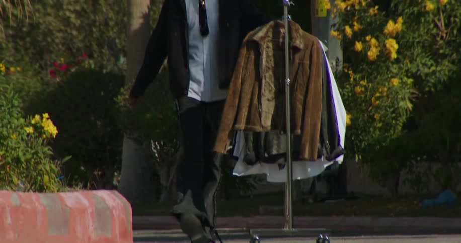 A young man pushes a clothing rack down a street