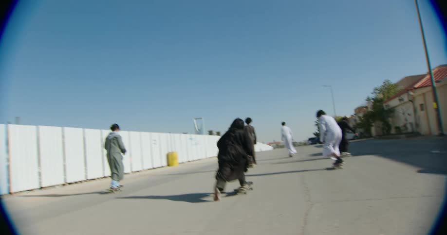 A group of people wearing thobes skateboarding down the street