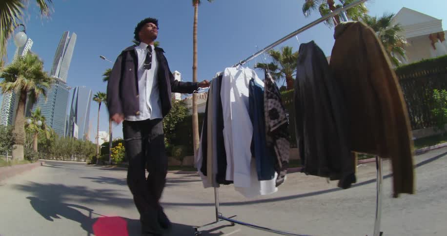 Man in a tie and jacket walking through the streets of a neighborhood in the metropolitan city carrying hangers of fashion clothes with him