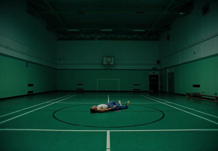 Person lying down in the center of a sports court moving their arms while dancing