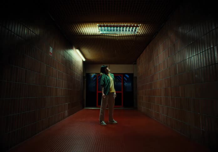 A woman standing in the center of a dimly lit hallway dances with twitchy movements