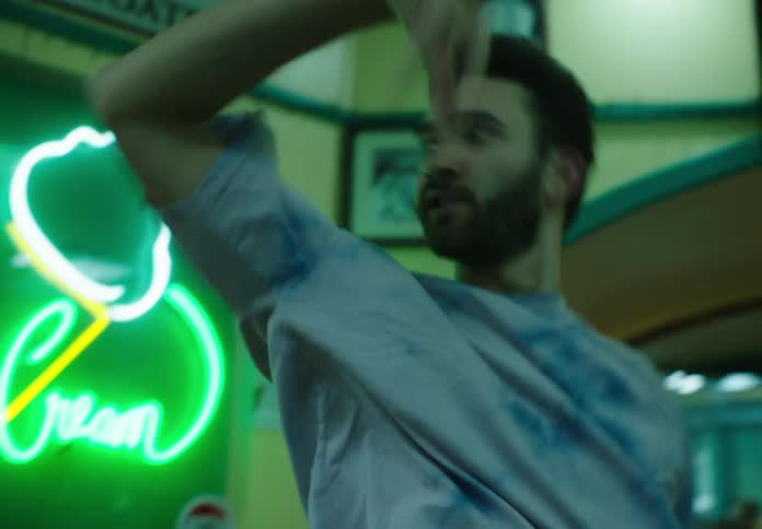 A bearded man wearing a blue tshirt dances in front of a green led light in a room