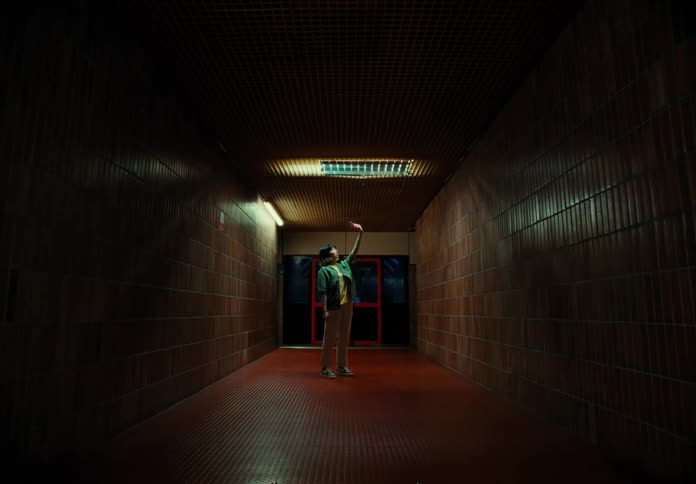 A person stands in a dimly lit corridor facing up with a hand exteded to the ceiling