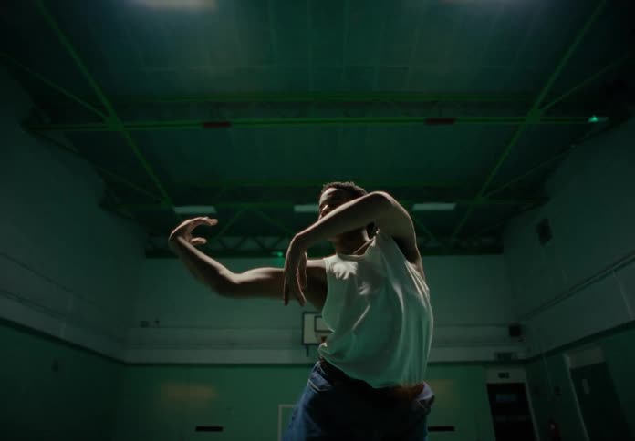 A black man dances in a darkened gym