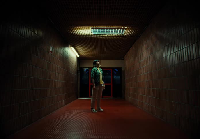 A woman stands in a hallway with red walls and then moves her head quickly