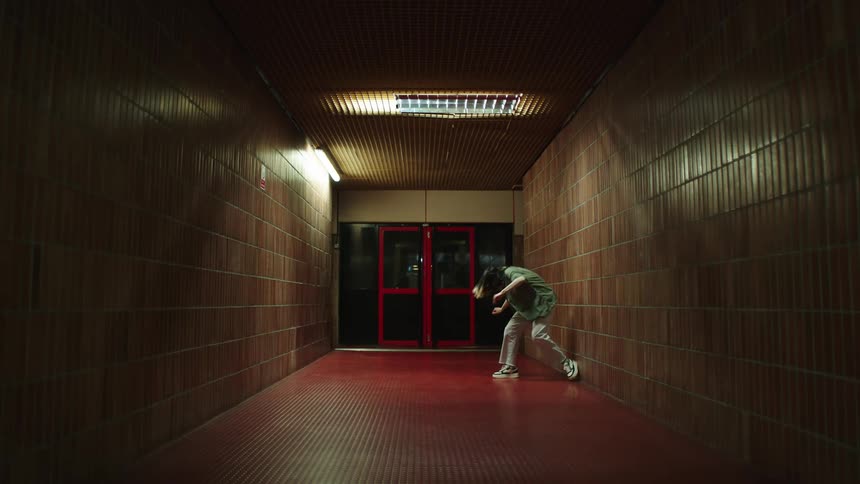 Woman wearing a green shirt and beige pants dances in the corridor