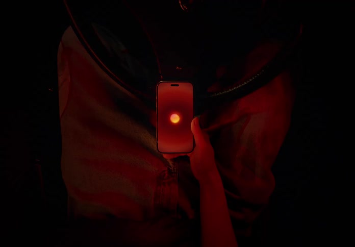 A closeup of a hand holding a smartphone with its screen illuminated on a subtle red lighting