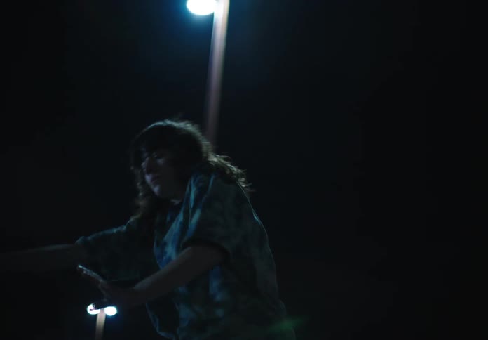 Woman with wavy hair a blue shirt and pants dances in the public park at night