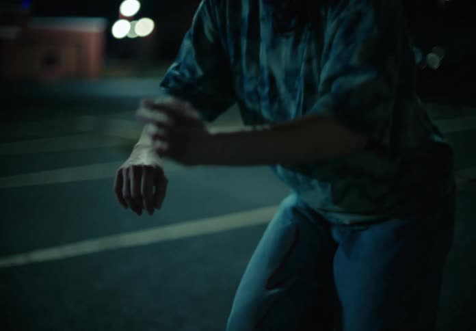 Woman with wavy hair a blue t shirt and jeans dances on the street at night