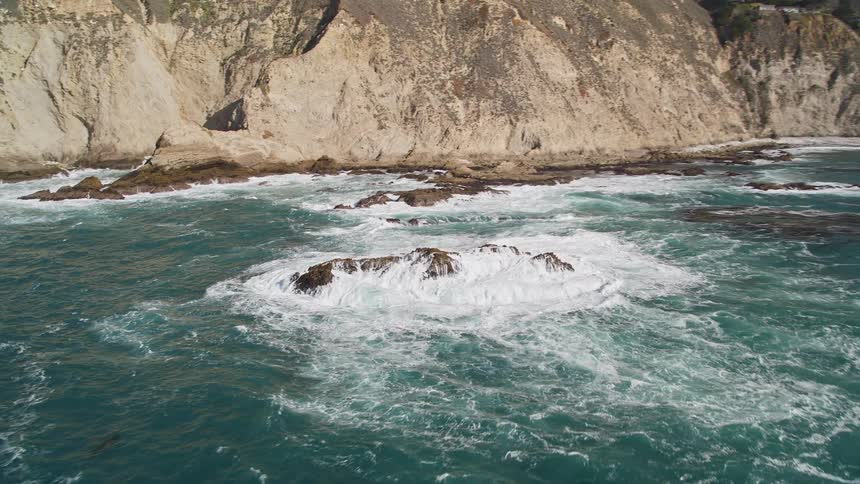 Powerful waves crash against the rocky coastline sending plumes of mist into the air
