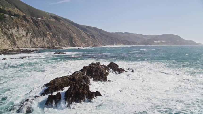 Powerfully crashing waves churn the ocean into a foamy frenzy sending spray high into the air as they meet the rocky shoreline on a sunny day