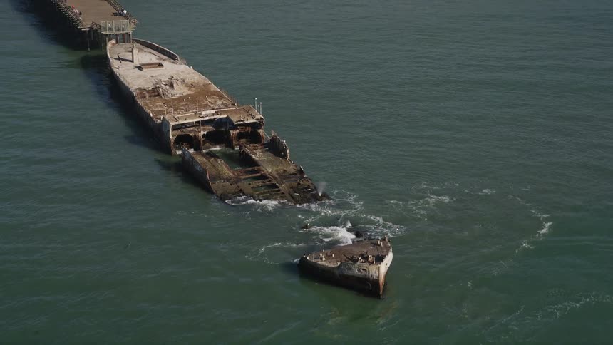 Aerial scenery of a beach with a dock that leads to a docked ship