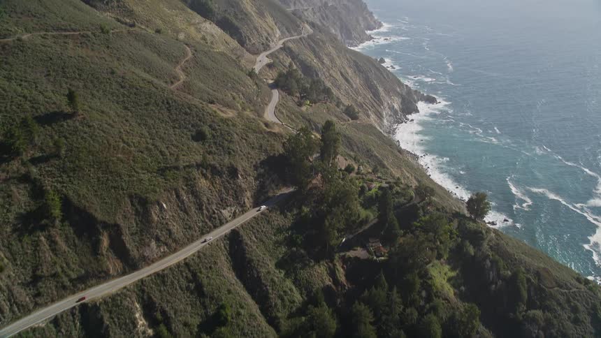 A winding road snakes along a dramatic coastline with cliffs that plunge down to a turquoise ocean