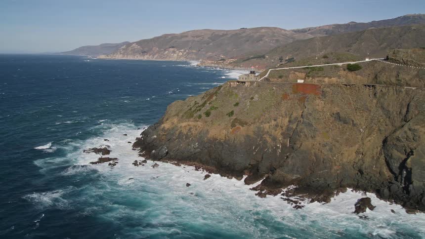 The white house with a red roofsits perched on a cliff overlooking a vast blue ocean