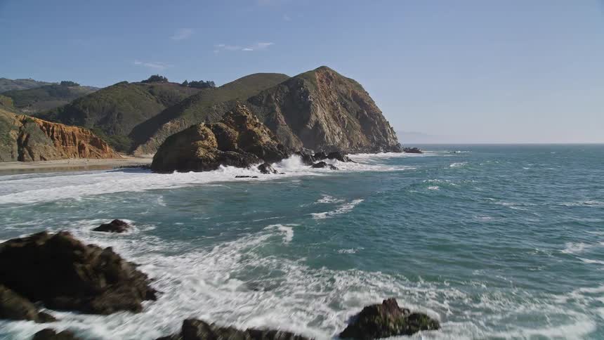 Aerial view of giant waves crashing against the rocky shoreline creating a frothy white spray