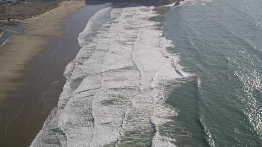 Waves foam while hitting the beach on both sides of mound and river inlet
