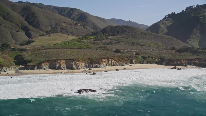 Aerial landscape of smoky waves on a beach with rocky coast and mountain ranges