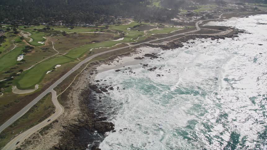 Aerial panorama of a beach with strong waves reaching the edge of a highway on the edge of mountains on a peninsula