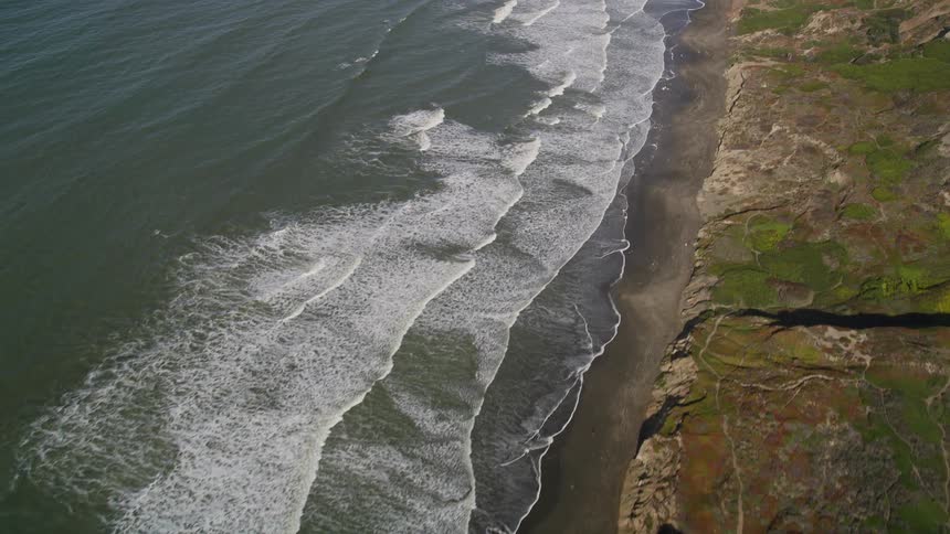 Aerial panorama of foamy sea waves crashing against a rugged land cliff