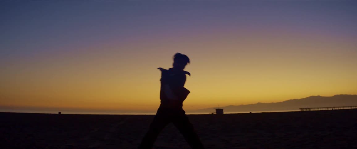 Man dances on the beach after dusk silhouetted against the afterglow filling the sky