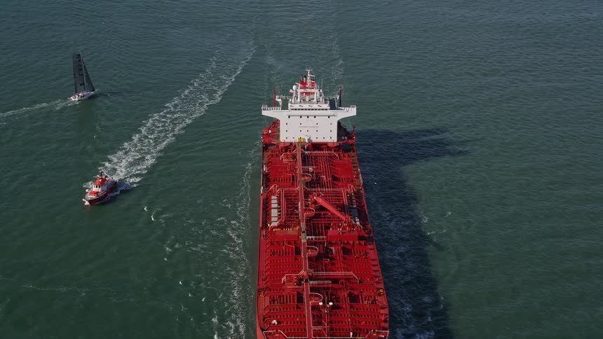 A huge orange cargo ship sailing on the water and behind it is a large bridge