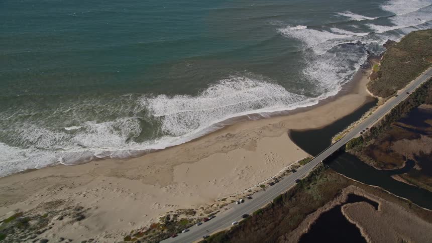 The winding coastal road snakes along the edge of a secluded beach with turquoise water lapping at the shore