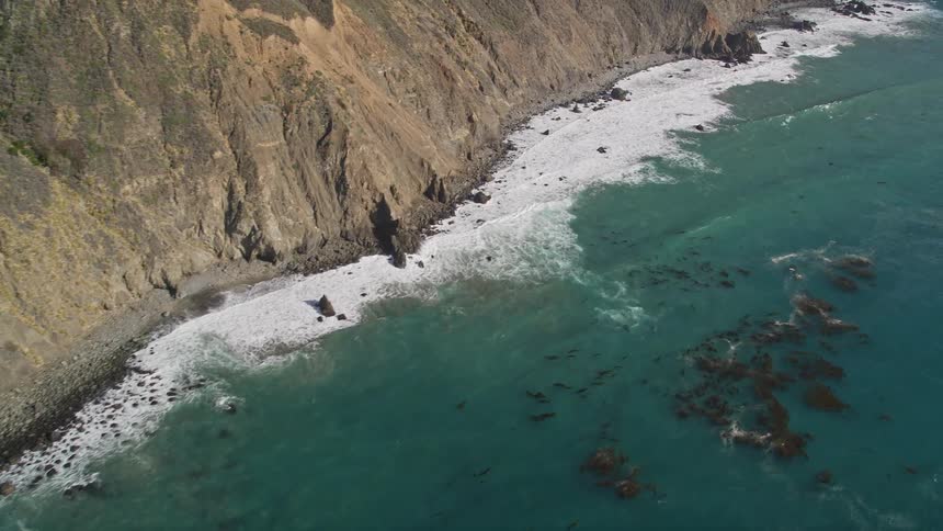 Aerial view of rocks submerged near the beach of a mountainous coastline