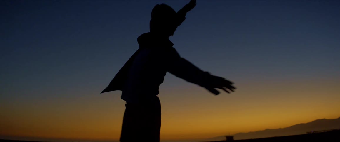 Silhouette of a person dancing on the beach with mountains on the horizon against a blue and yellow sky