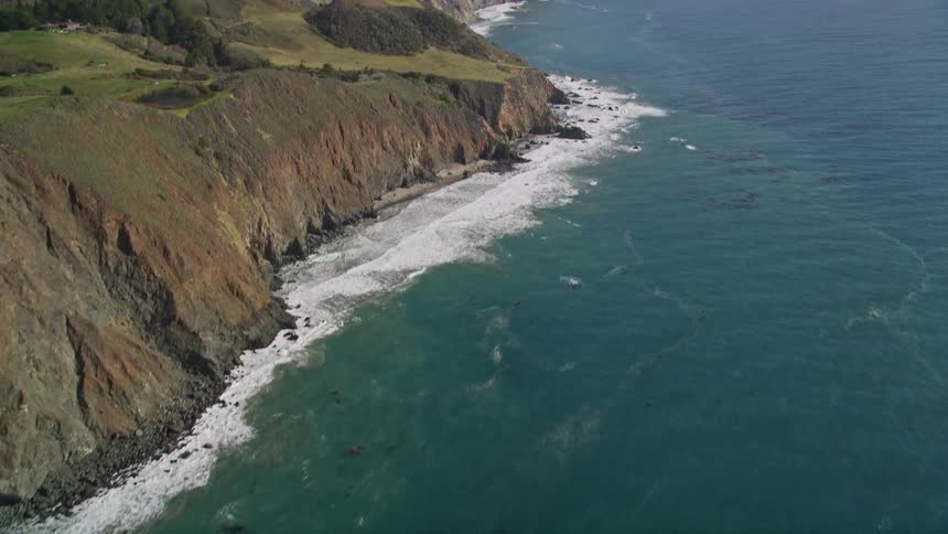 Foaming waves separate seaside cliffs from blue green ocean waters