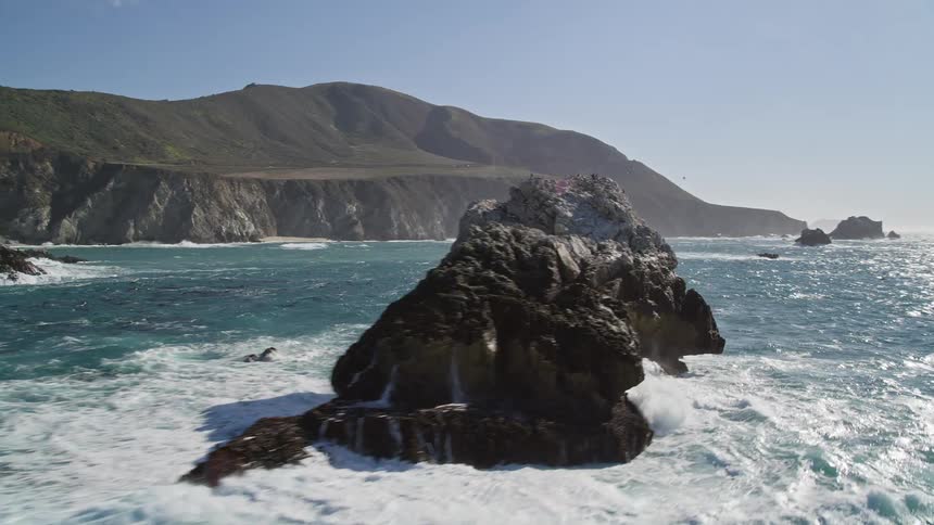 Rock formations stand in ocean water across from coastal bridge