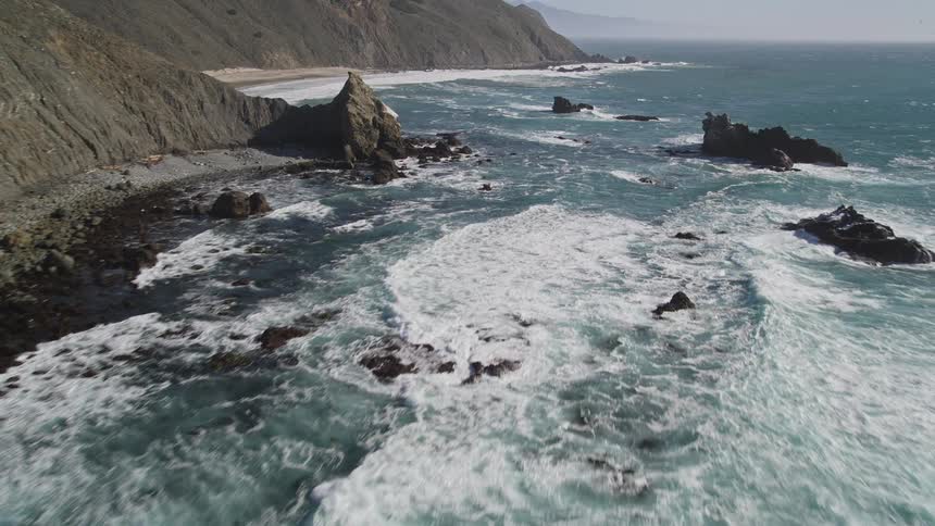 Landscape of an extensive ocean with foamy waves reaching the rocky shore