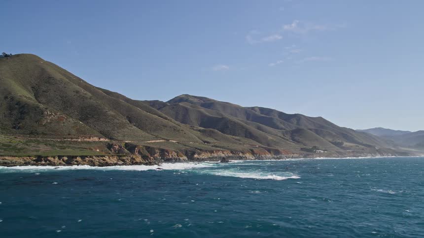 Aerial view of a coastal landscape with rolling hills descending into the sea