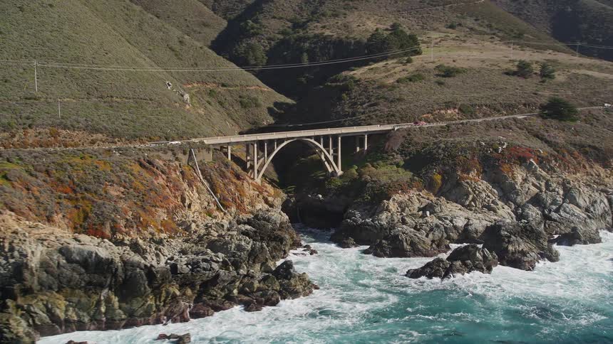 Traffic crosses arched bridge on mountainous coast